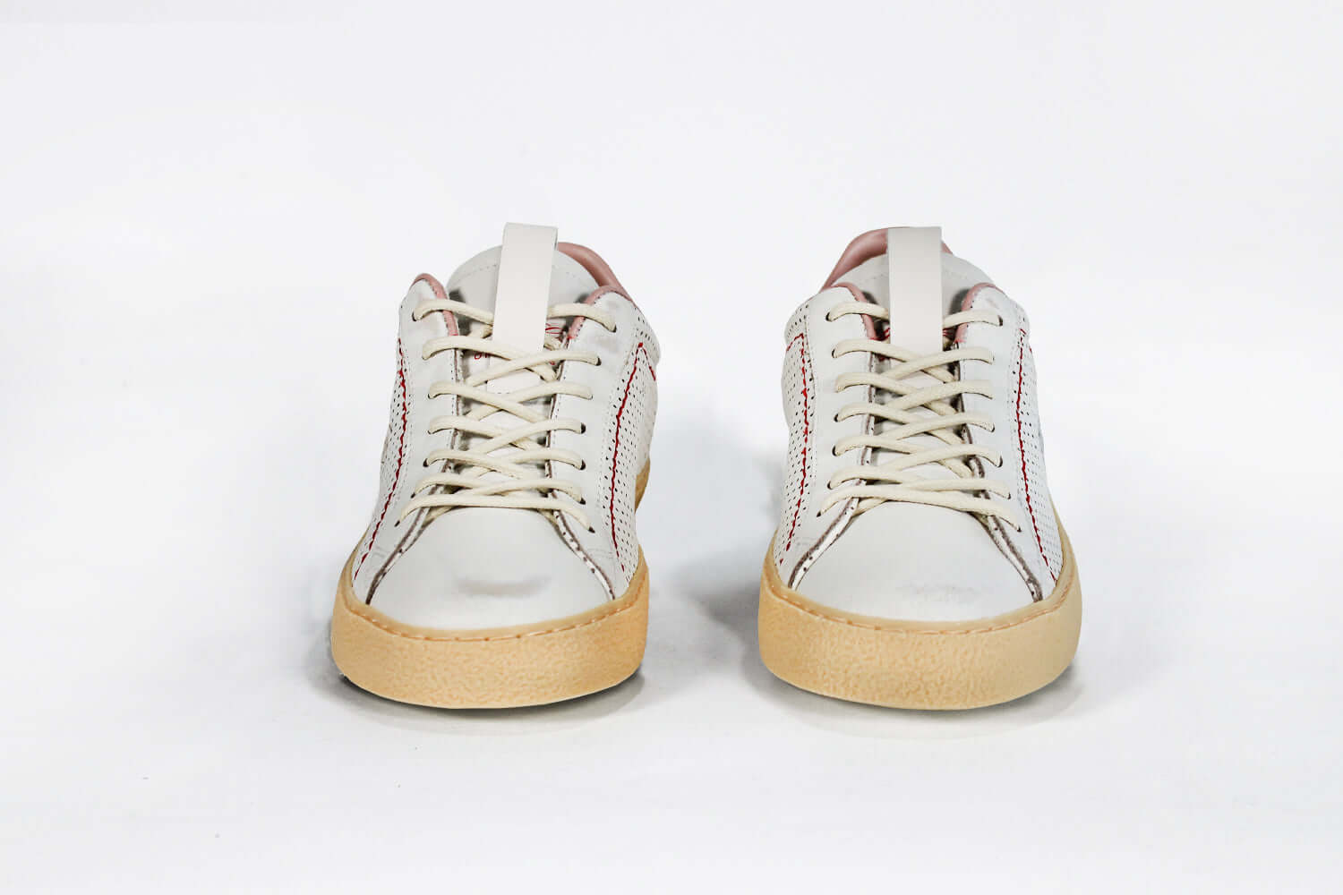 Front view of low top perforated aged white leather sneaker with blush pink accents, red stitching detail and pale natural rubber sole.