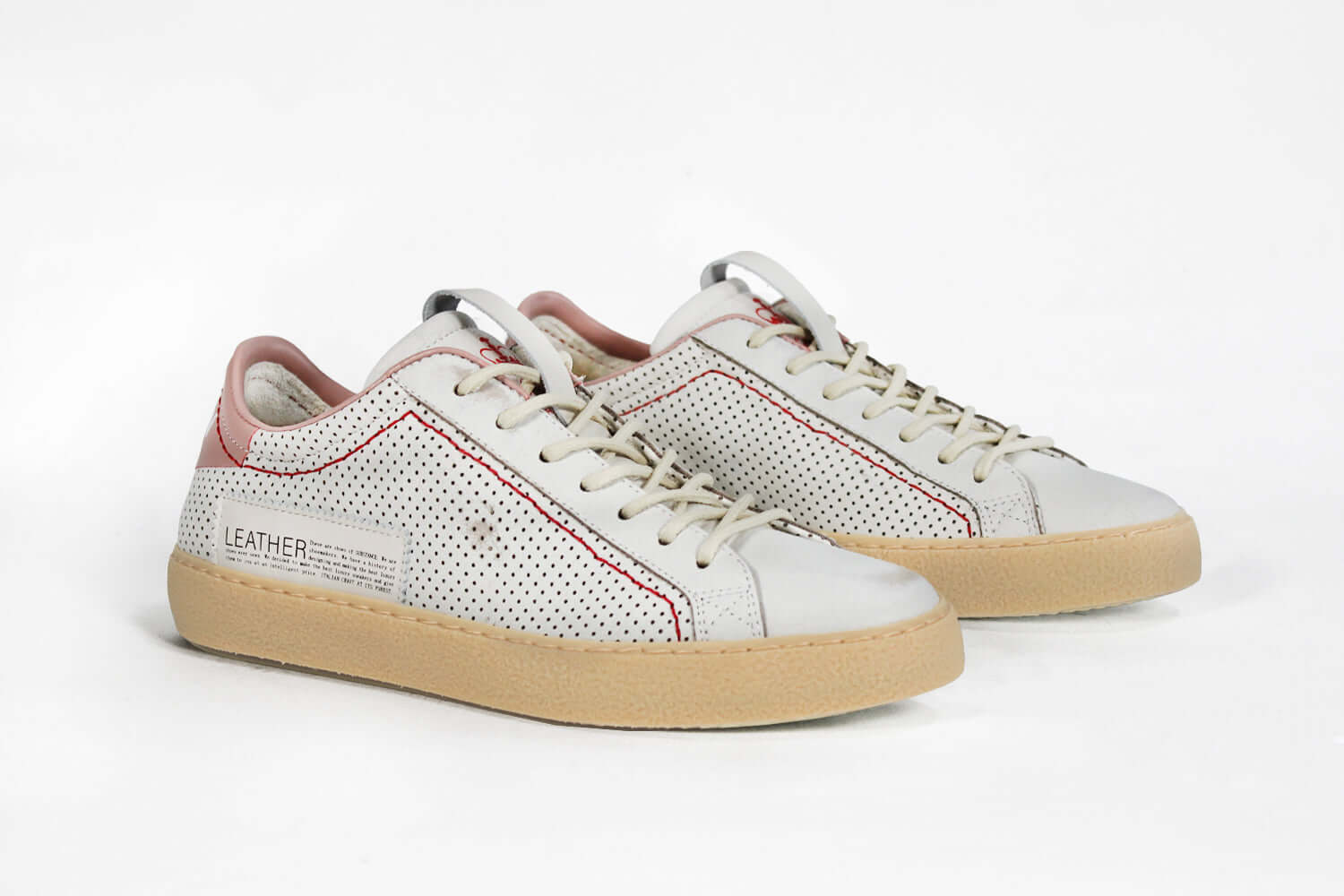 Three quarter front view of low top perforated aged white leather sneaker with blush pink accents, red stitching detail and pale natural rubber sole.