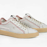 Three quarter front view of low top perforated aged white leather sneaker with blush pink accents, red stitching detail and pale natural rubber sole.