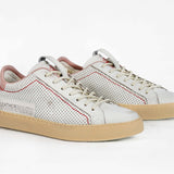 Three quarter front view of low top perforated aged white leather sneaker with blush pink accents, red stitching detail and pale natural rubber sole.