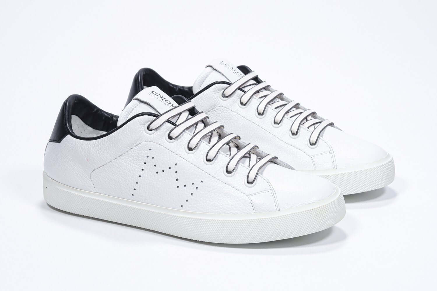 Vue de trois quarts d'un modèle bas blanc sneaker avec des détails noirs et le logo perforé de la couronne sur la tige. Tige en cuir et semelle en caoutchouc blanc.
