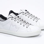 Three quarter view of low top white sneaker with black detailing and perforated crown logo on upper. Full leather upper and white rubber sole.