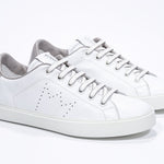 Three quarter front view of low top white sneaker with beige detailing and perforated crown logo on upper. Full leather upper and white rubber sole.