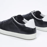 Three quarter back view of low top black sneaker with white detailing and perforated crown logo on upper. Full leather upper and white rubber sole.