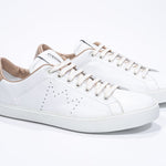 Three quarter front view of low top white sneaker with cuoio detailing and perforated crown logo on upper. Full leather upper and white rubber sole.