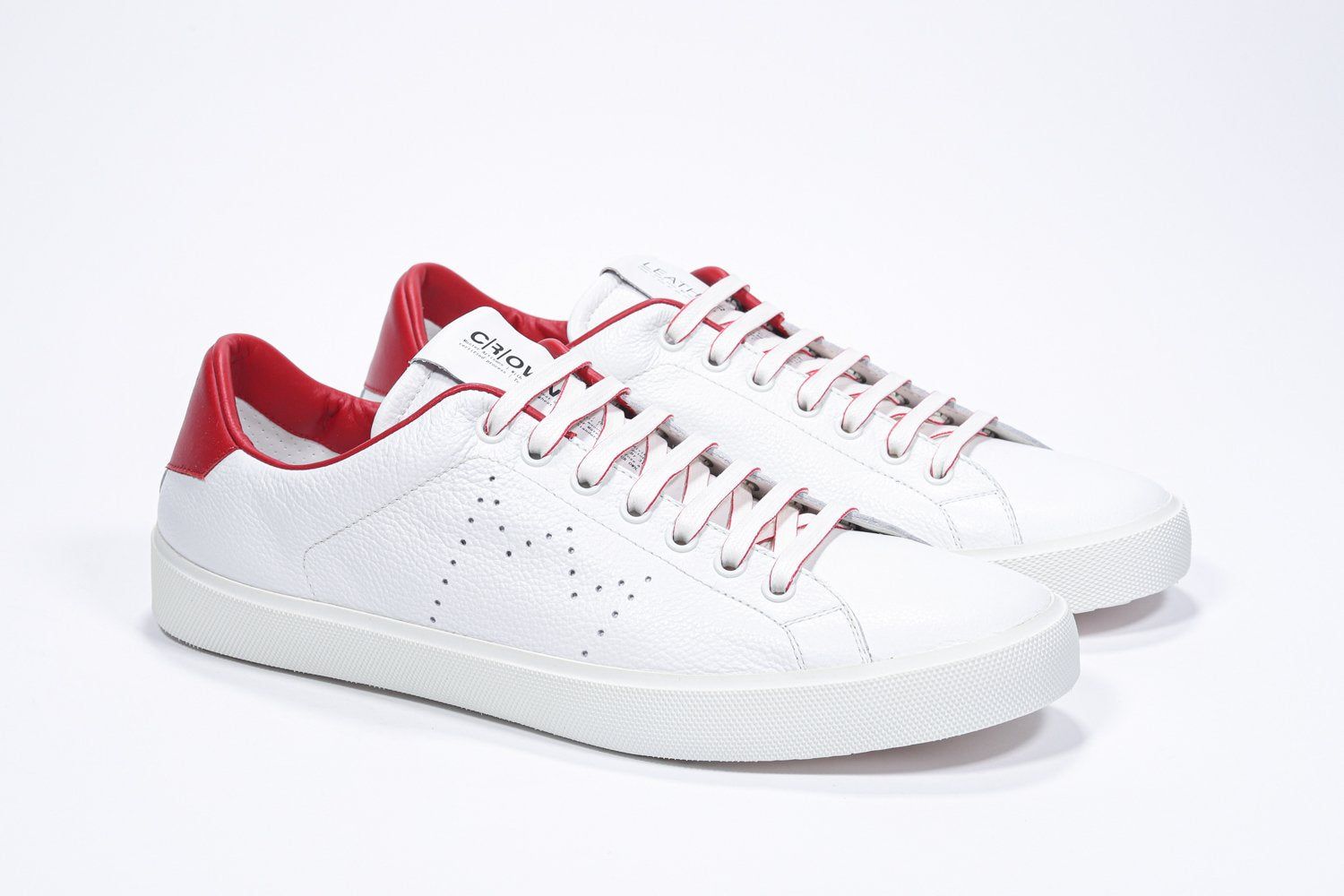 Three quarter front view of low top white sneaker with red detailing and perforated crown logo on upper. Full leather upper and white rubber sole.