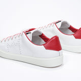 Three quarter back view of low top white sneaker with red detailing and perforated crown logo on upper. Full leather upper and white rubber sole.