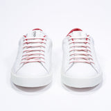 Front view of low top white sneaker with red detailing and perforated crown logo on upper. Full leather upper and white rubber sole.