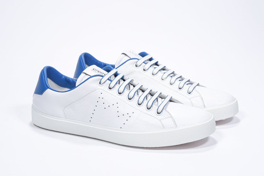 Three quarter front view of low top white sneaker with blue detailing and perforated crown logo on upper. Full leather upper and white rubber sole.