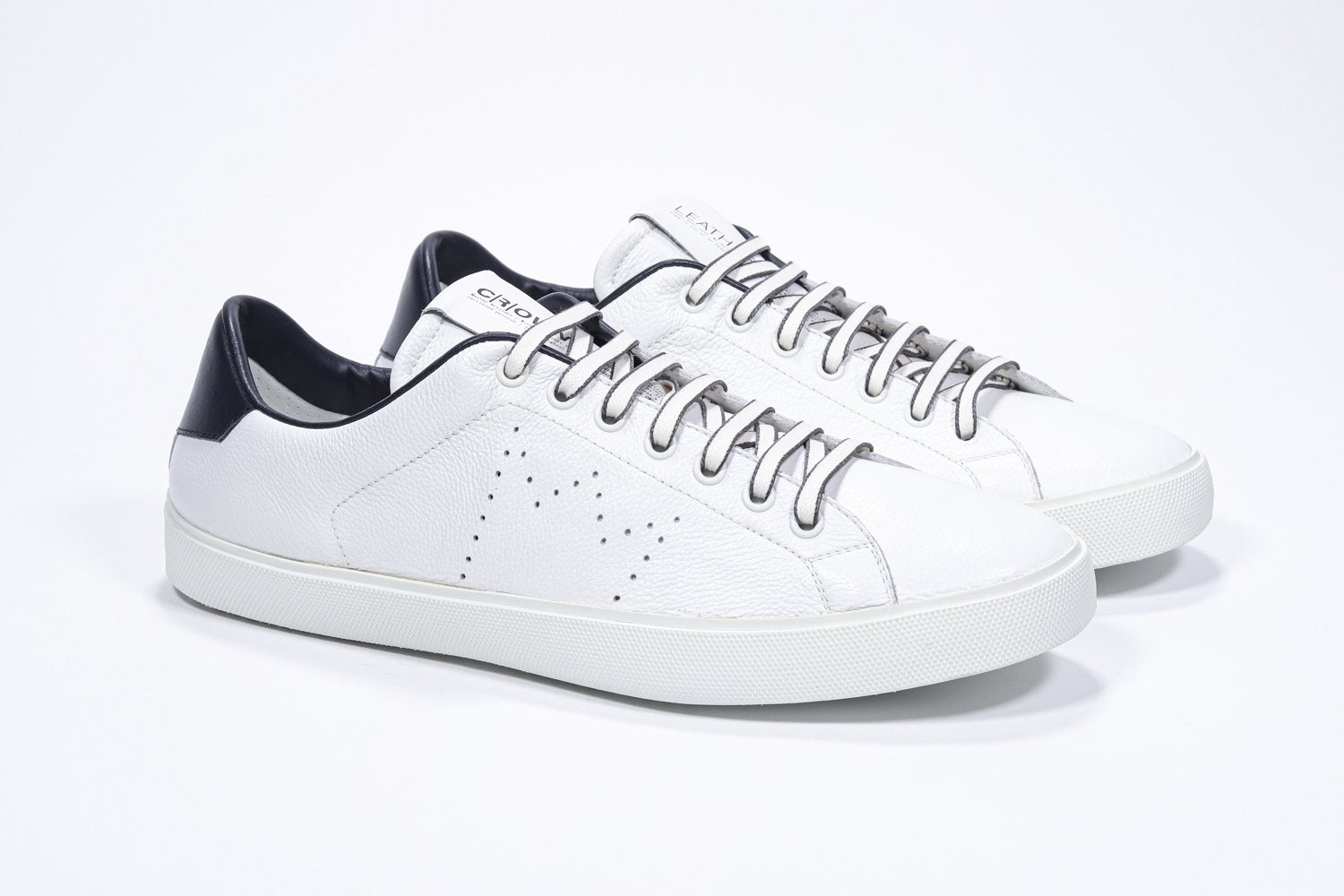 Vue de trois quarts de l'avant de la chaussure blanche sneaker avec des détails en bleu marine et le logo perforé de la couronne sur l'empeigne. Tige en cuir et semelle en caoutchouc blanc.