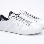 Three quarter front view of low top white sneaker with navy detailing and perforated crown logo on upper. Full leather upper and white rubber sole.