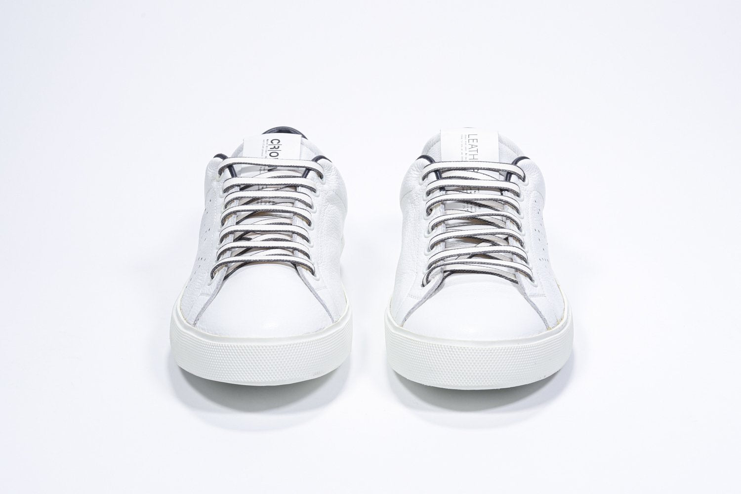 Front view of low top white sneaker with navy detailing and perforated crown logo on upper. Full leather upper and white rubber sole.