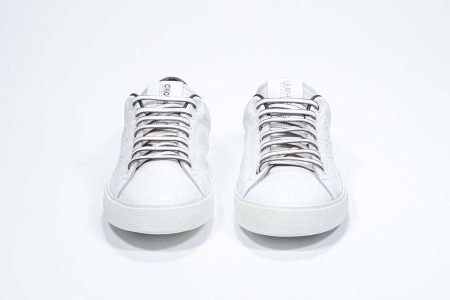 Front view of low top white sneaker with navy detailing and perforated crown logo on upper. Full leather upper and white rubber sole.