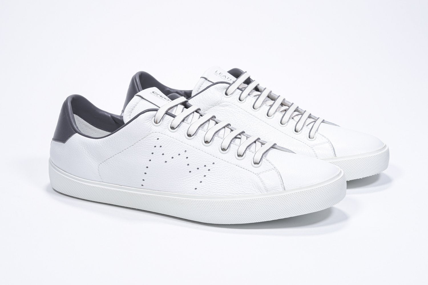 Three quarter front view of low top white sneaker with dark grey detailing and perforated crown logo on upper. Full leather upper and white rubber sole.