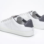 Three quarter back view of low top white sneaker with dark grey detailing and perforated crown logo on upper. Full leather upper and white rubber sole.