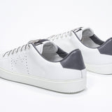 Three quarter back view of low top white sneaker with dark grey detailing and perforated crown logo on upper. Full leather upper and white rubber sole.