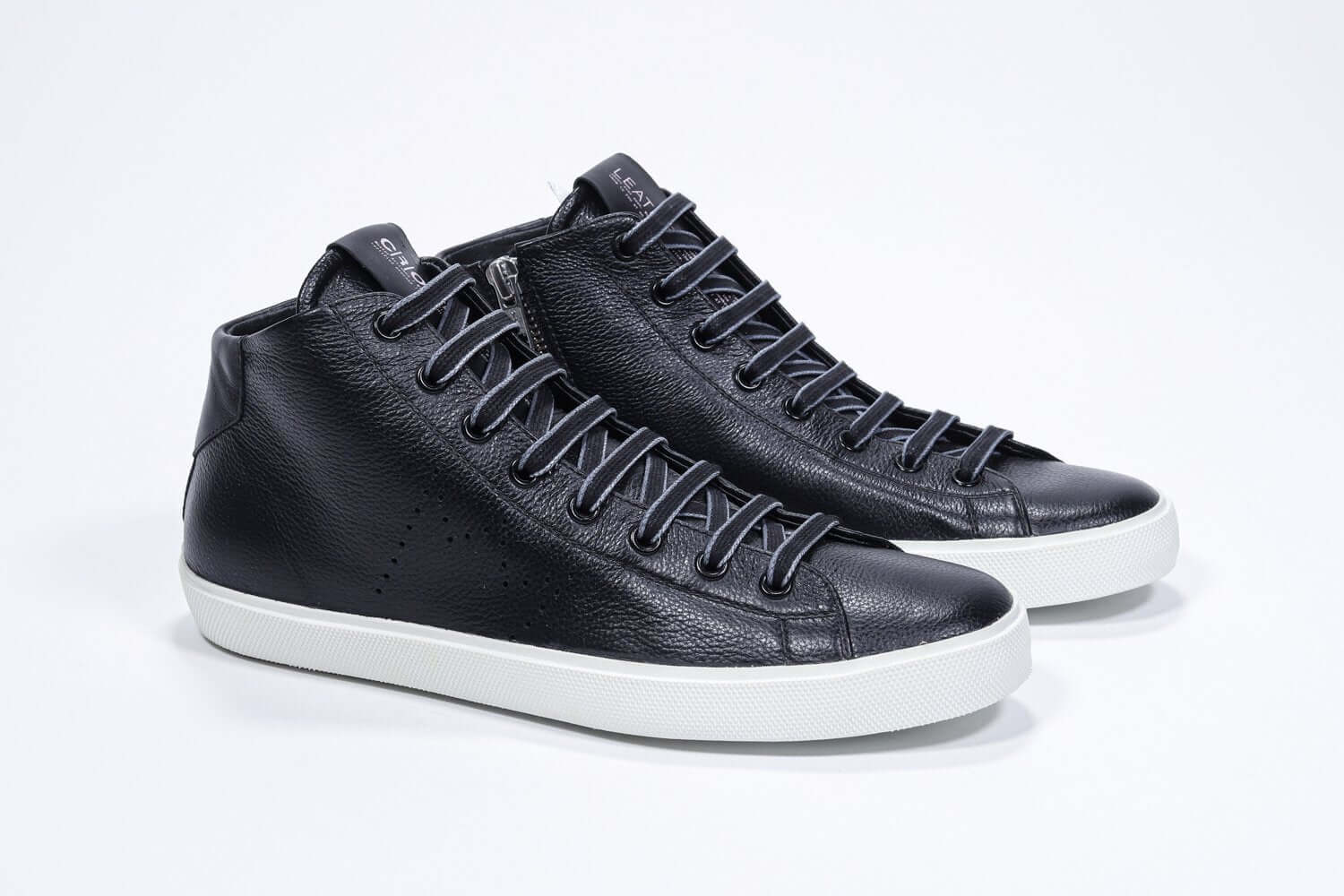 Vue de trois quarts de l'avant de la chaussure de sport noire sneaker avec une tige en cuir avec un logo perforé, une fermeture éclair interne et une semelle blanche.