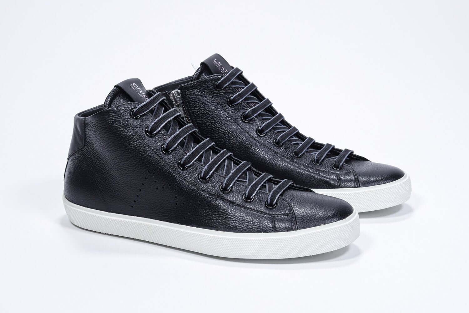Three quarter front view of mid top black sneaker with full leather upper with perforated crown logo, internal zip and white sole.