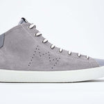 Side profile of mid top light grey sneaker with full suede upper with perforated crown logo, internal zip and white sole.