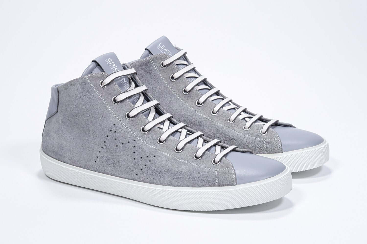 Vue de trois quarts de l'avant de la chaussure gris clair sneaker avec une tige en daim, un logo perforé, une fermeture éclair interne et une semelle blanche.