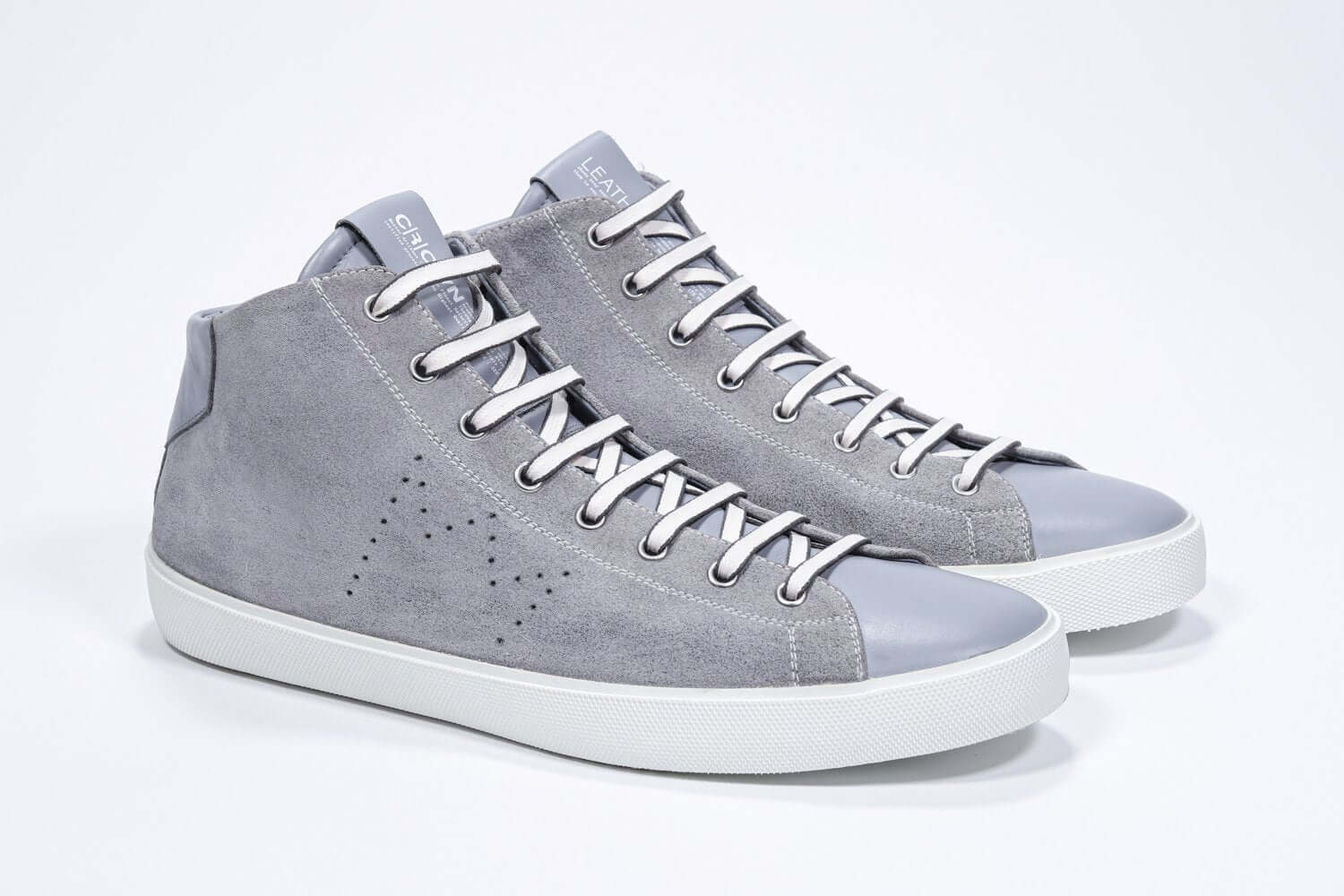 Three quarter front view of mid top light grey sneaker with full suede upper with perforated crown logo, internal zip and white sole.