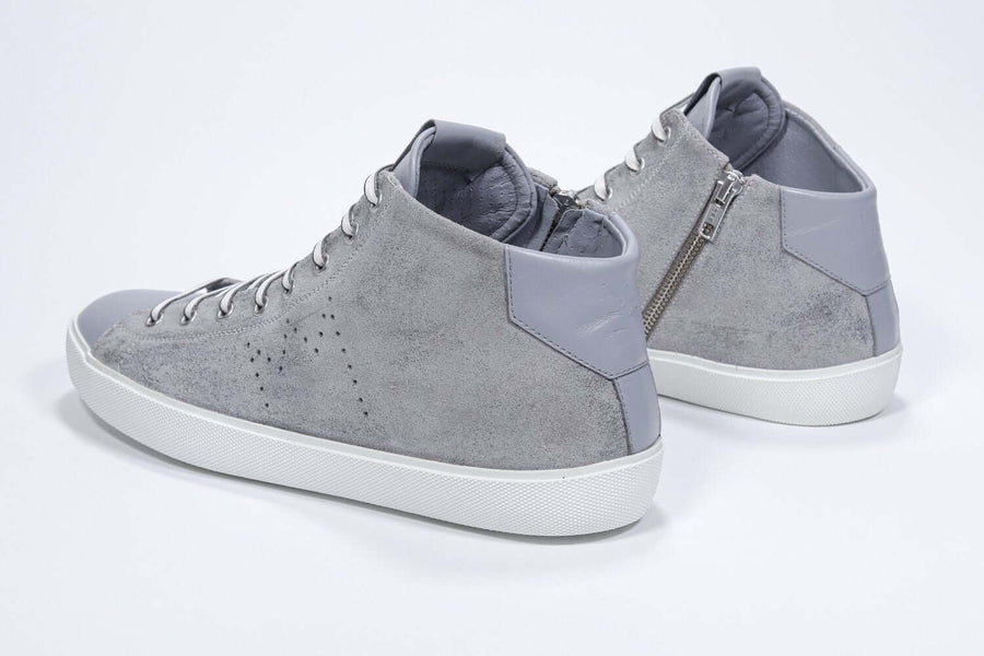 Three quarter back view of mid top light grey sneaker with full suede upper with perforated crown logo, internal zip and white sole.