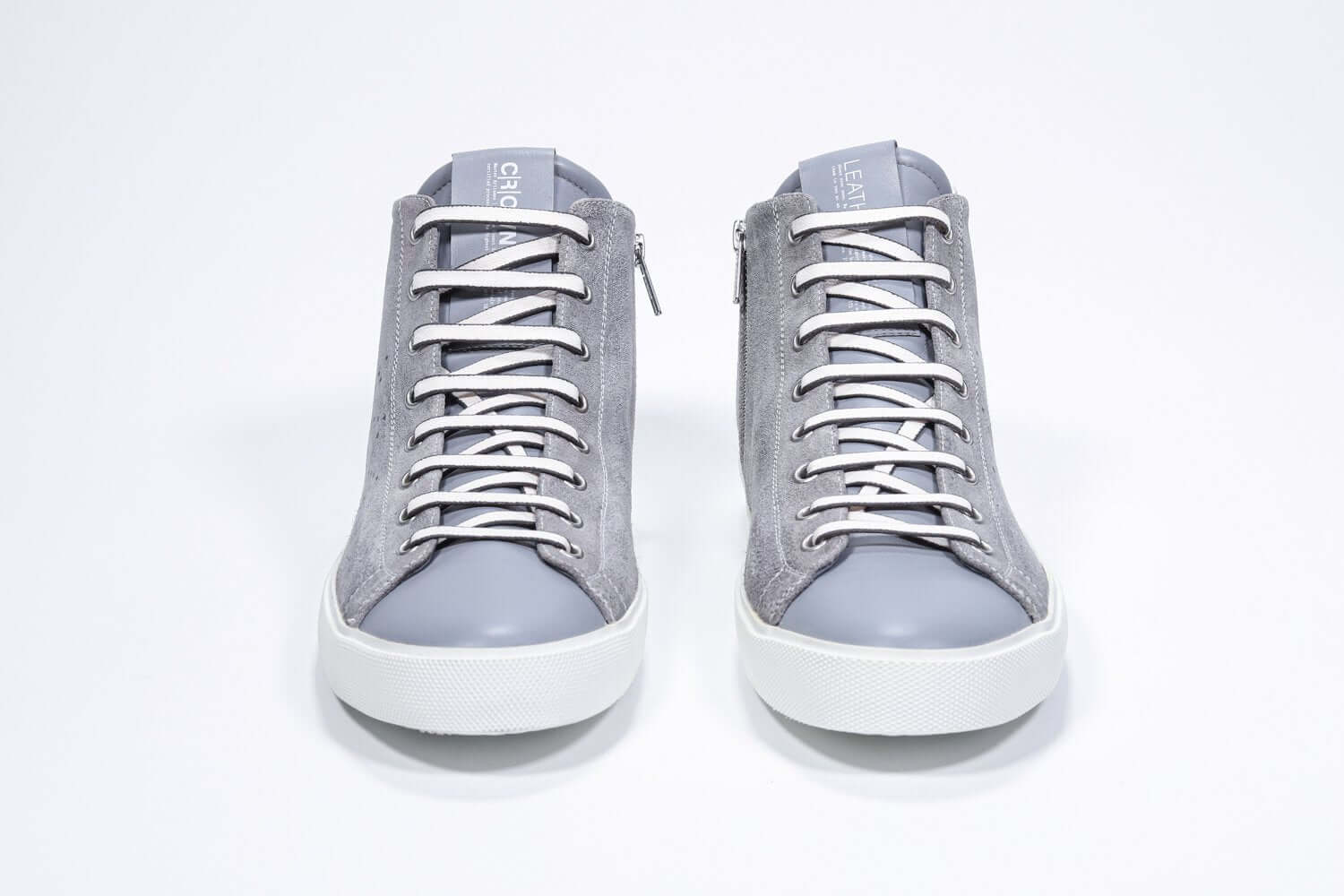 Vue de face du modèle mid top gris clair sneaker à tige entièrement en daim avec logo perforé, fermeture à glissière interne et semelle blanche.