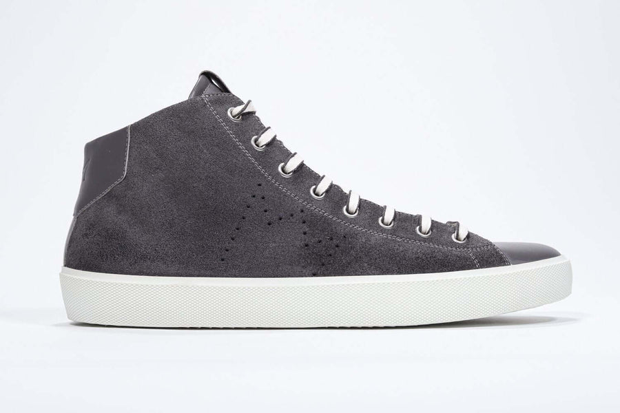 Side profile of mid top dark grey sneaker with full suede upper with perforated crown logo, internal zip and white sole.