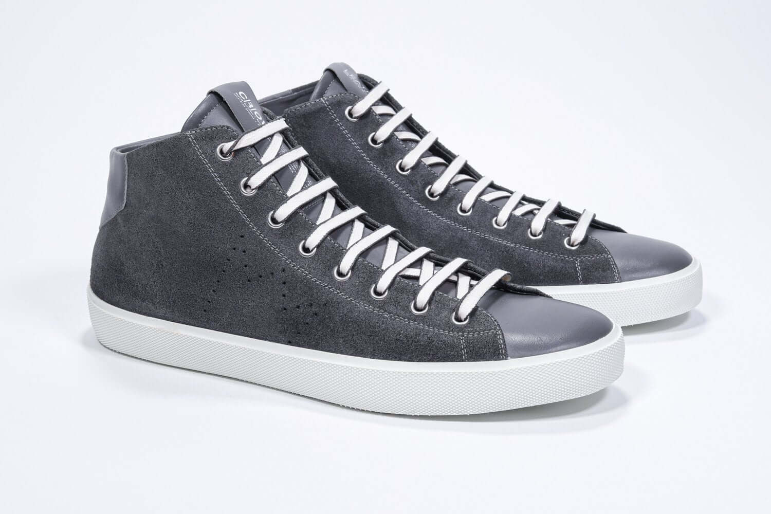 Vue de trois quarts avant du modèle mid top gris foncé sneaker à tige entièrement en daim avec logo perforé, fermeture à glissière interne et semelle blanche.