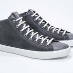 Three quarter front view of mid top dark grey sneaker with full suede upper with perforated crown logo, internal zip and white sole.