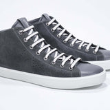 Three quarter front view of mid top dark grey sneaker with full suede upper with perforated crown logo, internal zip and white sole.