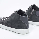 Three quarter back view of mid top dark grey sneaker with full suede upper with perforated crown logo, internal zip and white sole.