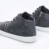 Three quarter back view of mid top dark grey sneaker with full suede upper with perforated crown logo, internal zip and white sole.