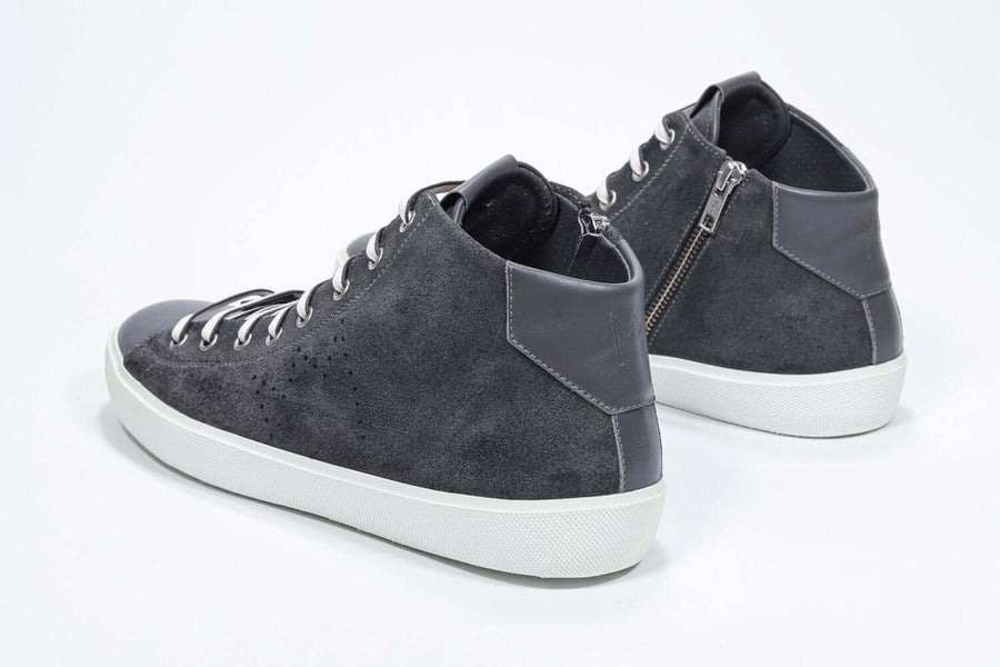 Three quarter back view of mid top dark grey sneaker with full suede upper with perforated crown logo, internal zip and white sole.