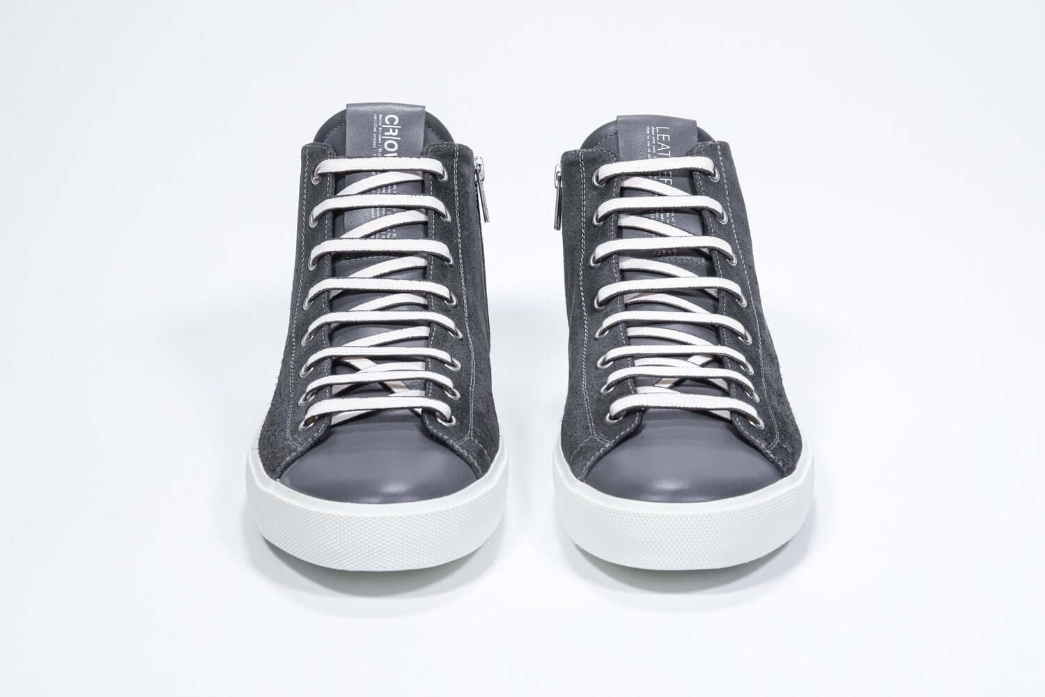 Vue de face du modèle mid top gris foncé sneaker à tige entièrement en daim avec logo perforé, fermeture à glissière interne et semelle blanche.