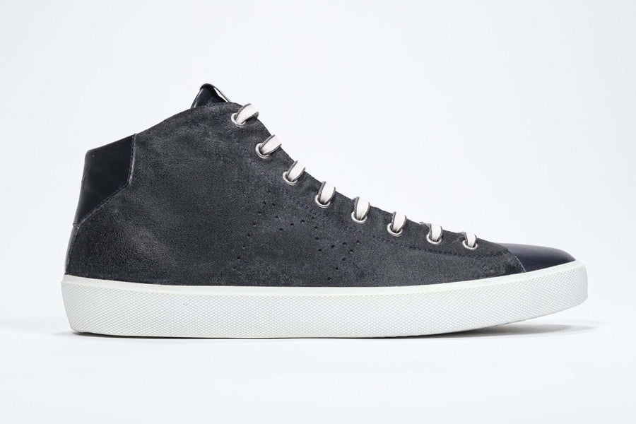 Side profile of mid top navy sneaker with full suede upper with perforated crown logo, internal zip and white sole.