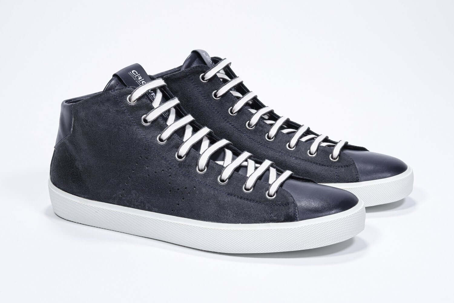 Three quarter front view of mid top navy sneaker with full suede upper with perforated crown logo, internal zip and white sole.
