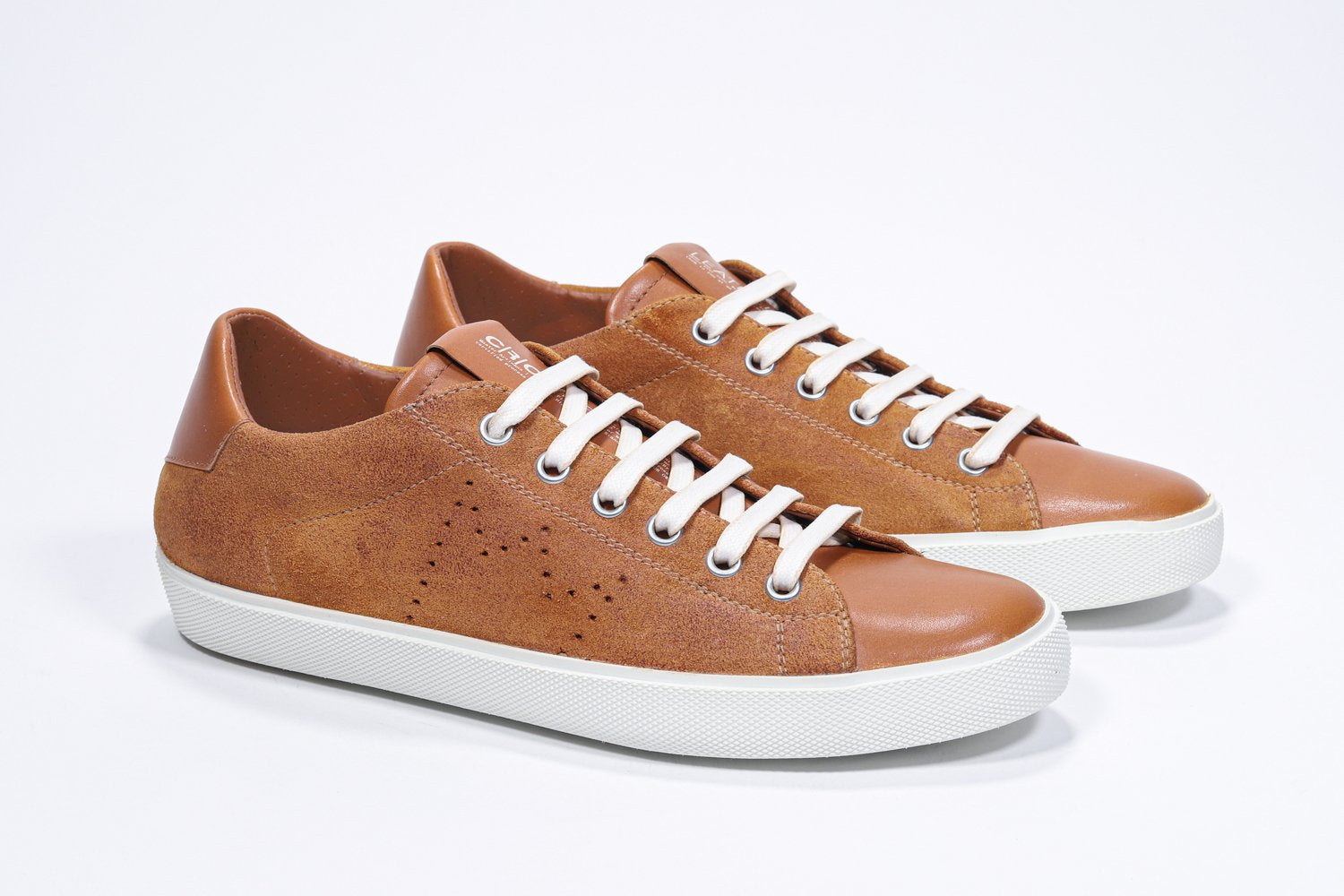 Three quarter front view of low top sneaker with perforated crown logo on upper. Full rust suede upper and white rubber sole.