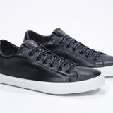 Three quarter front view of low top black sneaker with perforated crown logo on upper. Full leather upper and white rubber sole.