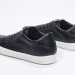 Three quarter back view of low top black sneaker with perforated crown logo on upper. Full leather upper and white rubber sole.