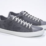 Three quarter front view of low top dark grey sneaker with perforated crown logo on upper. Full suede upper and white rubber sole.