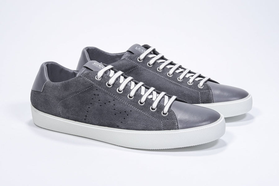 Three quarter front view of low top dark grey sneaker with perforated crown logo on upper. Full suede upper and white rubber sole.