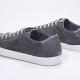 Three quarter back view of low top dark grey sneaker with perforated crown logo on upper. Full suede upper and white rubber sole.