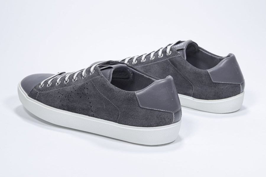 Three quarter back view of low top dark grey sneaker with perforated crown logo on upper. Full suede upper and white rubber sole.
