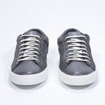Vue de face de la chaussure basse gris foncé sneaker avec logo perforé sur la tige. Tige en daim et semelle en caoutchouc blanc.