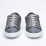 Vue de face de la chaussure basse gris foncé sneaker avec logo perforé sur la tige. Tige en daim et semelle en caoutchouc blanc.