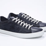 Three quarter front view of low top navy sneaker with perforated crown logo on upper. Full suede upper and white rubber sole.