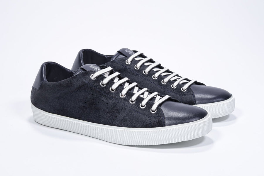 Three quarter front view of low top navy sneaker with perforated crown logo on upper. Full suede upper and white rubber sole.