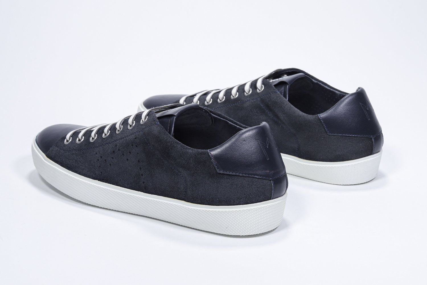 Three quarter back view of low top navy sneaker with perforated crown logo on upper. Full suede upper and white rubber sole.