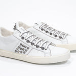 Three quarter front view of low top white sneaker. Full leather upper with studs and vintage rubber sole.